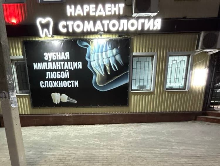 Здание стоматологии Наре Дент в Белёве, вид с улицы ночью: фасад здания, светящаяся вывеска «Наредент Стоматология» и рекламный баннер.