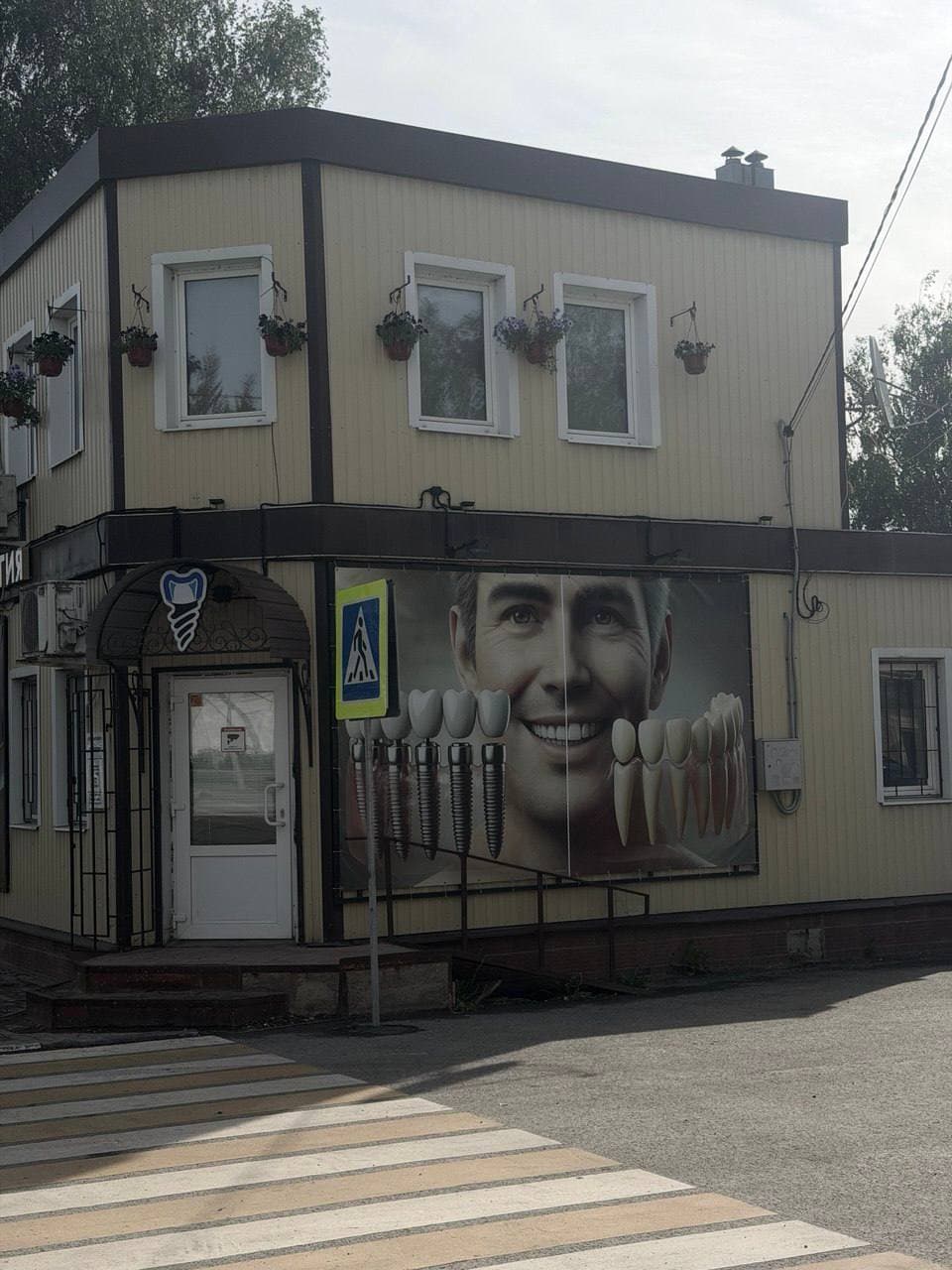 Стоматология «Наре Дент» в Белёве: фасад клиники днём, вход слева, пешеходный переход и крупный баннер на стене.
